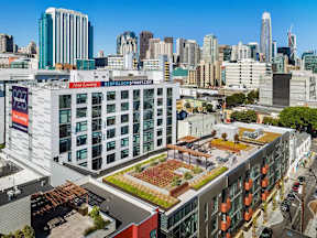 A view of a city with a building that has a green roof and a sign that says "New Apartments".