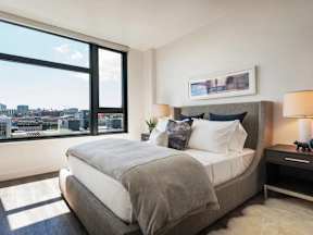 A bedroom with a large bed and a city view through the window.