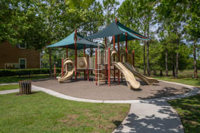 a playground with two slides and two umbrellas at the whispering winds apartments in pearland
