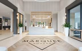 A reception area with a white reception desk and a rug that says Marquee Square.