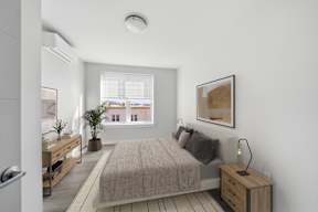 A bedroom with a bed, nightstand, and a window overlooking a cityscape.