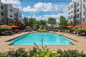 a swimming pool with lounge chairs and umbrellas in front of an apartment building