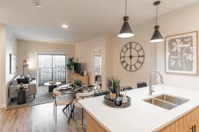 A modern kitchen with a dining table and chairs, a clock on the wall, and pendant lights hanging above the island.at Vista Apartments at Edgemont, Edmonton, T6M 1J4