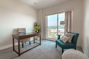 A room with a desk, chair, and window overlooking a balcony.