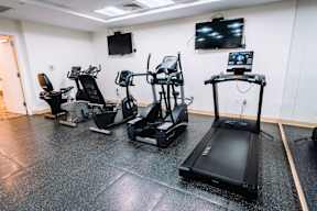A gym with treadmills, stationary bikes, and a television.