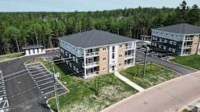 A parking lot in front of a building with a grassy area and trees in the background.