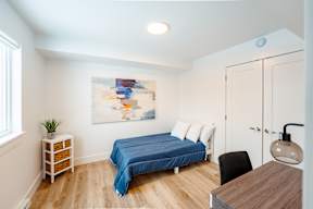 A bedroom with a blue bed and a painting on the wall.