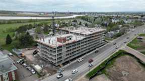 A large building under construction is surrounded by a busy road with cars.