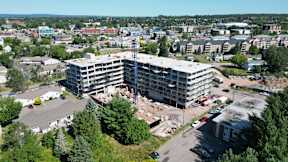A large building under construction is surrounded by trees and other buildings.