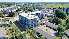 A large building under construction is surrounded by a parking lot and other buildings.