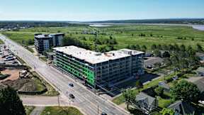 A large building with a green and white facade is under construction next to a busy road.