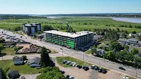 A large building with a green stripe is surrounded by a parking lot and other buildings.