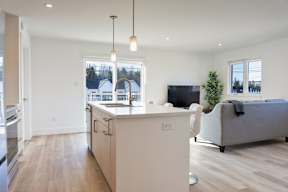 A modern kitchen with a white island and a grey couch in the living room.