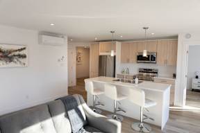A modern kitchen with a grey couch and white chairs.