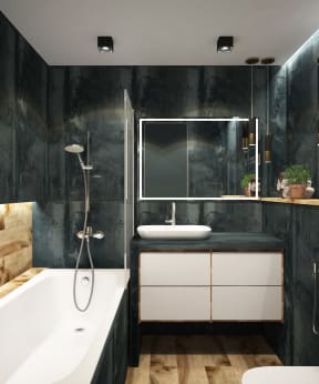 Master bathroom contains dark marble tile on the walls and countertop. There are also light hardwood floor and accent walls, white cabinets below the sink, and white porcelain fixtures. Bathtub contains a hand held shower head.