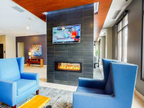 Two blue arm chairs next to floor to ceiling fireplace with TV mounted on top