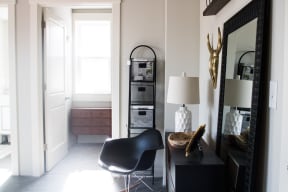 a corner of a room with a chair and a table with a lamp and a large mirror
