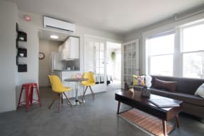 a living area with a couch coffee table and chairs and a small kitchen with a refrigerator and