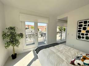 A bedroom with a bed, a potted plant, and a painting on the wall.