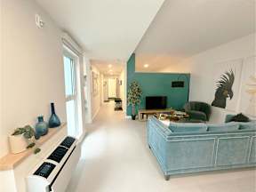 A blue couch sits in a bright living room with a white wall and a window.