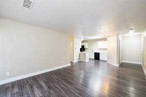 A spacious room with wood flooring and a kitchen area in the background.