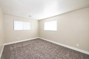 A room with carpeted floor and two windows.