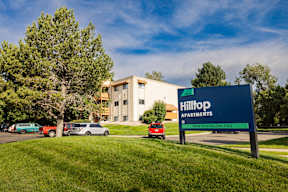 A sign for Hilltop Apartments is in front of a building and some trees.