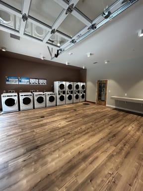 a washer and dryer room with wood floors and a row of washing machines