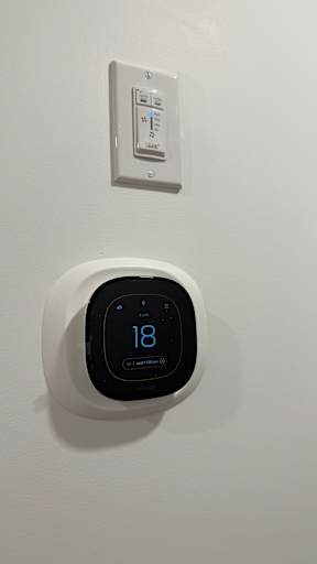 A wall-mounted thermostat with a digital display showing 18 degrees.