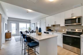 a kitchen with white cabinets and a large white island with blue chairs at shawnessy station