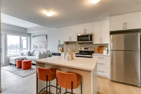 a kitchen with white cabinets and an island with three orange stools
