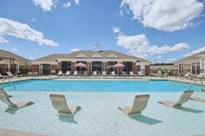 a large swimming pool with chairs and a building in the background