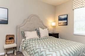 A bed with a blue and white patterned comforter sits in a room with a white wall and a window with blinds.