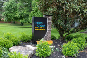a sign for toots creek village apartments in front of a garden