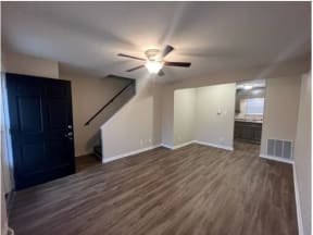 an empty living room with a ceiling fan and a kitchen in the background