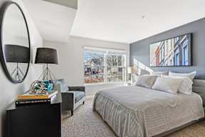 A bedroom with a large bed, a side table with a lamp, and a painting on the wall.