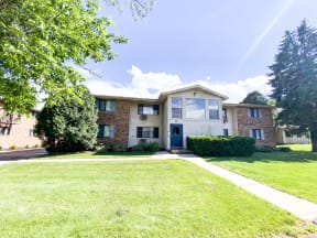 the view of an apartment building with a lawn and sidewalk in front of it