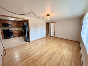 an empty living room with wood floors and a kitchen