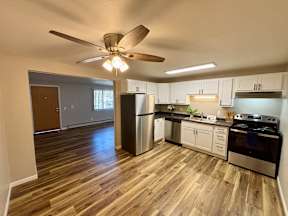 A kitchen with a stainless steel refrigerator, oven, and wooden flooring.