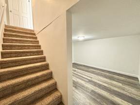 A staircase with a carpeted runner and wooden steps leads to a white door.