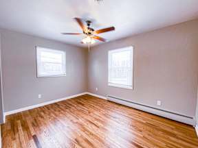 A room with a ceiling fan and two windows.
