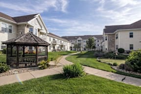 A gazebo sits in the middle of a grassy area in front of apartment buildings.