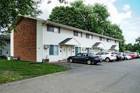 A parking lot with cars parked in front of a white building with a red brick chimney.