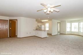 A spacious living room with a ceiling fan and carpeted floor.