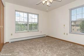A room with a carpeted floor, a ceiling fan, and two windows.