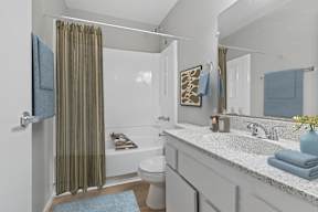 Updated bathroom in Oro apartment home with  wood-style plank flooring, white cabinetry, large vanity mirror and a shower/tub