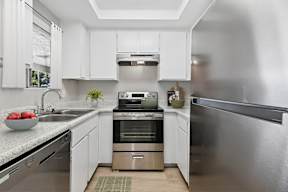 Modern updated kitchen in Oro Apartment home with wood-style plank flooring, stainless steel appliances, and white cabinetry.