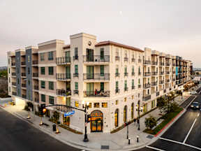 A street view of a row of apartment buildings with cars parked on the side of the road.