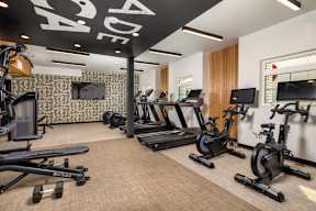 A gym with a variety of exercise equipment including treadmills, stationary bikes, and dumbbells.