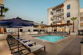 A pool area with sun loungers and umbrellas in front of a building.